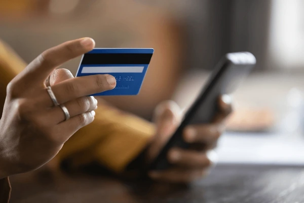 Hands holding a credit card with a mobile phone about to purchase something online.