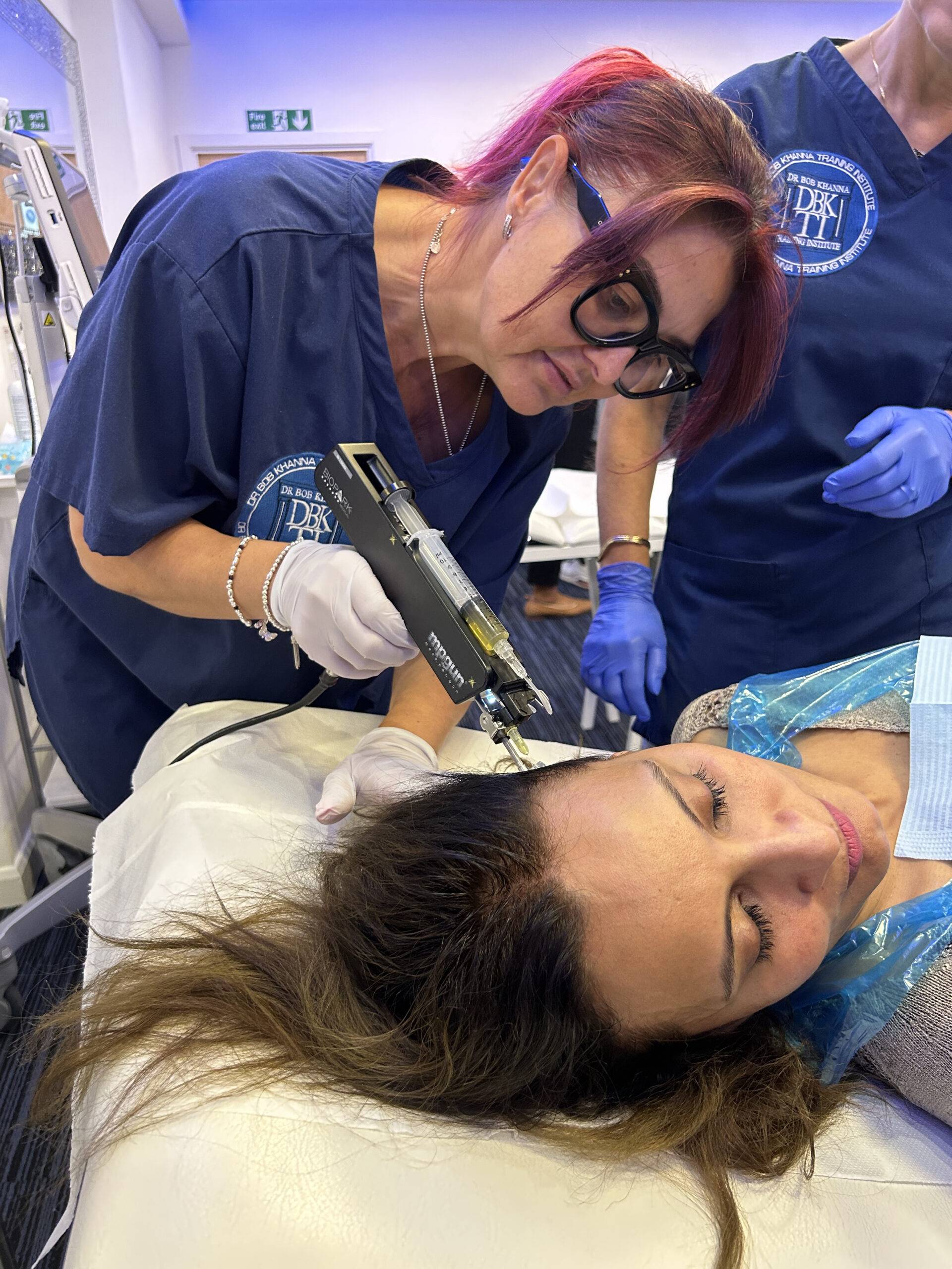 Image of a woman on a training course, injecting polynucleotides into a model's scalp for anti-hair loss