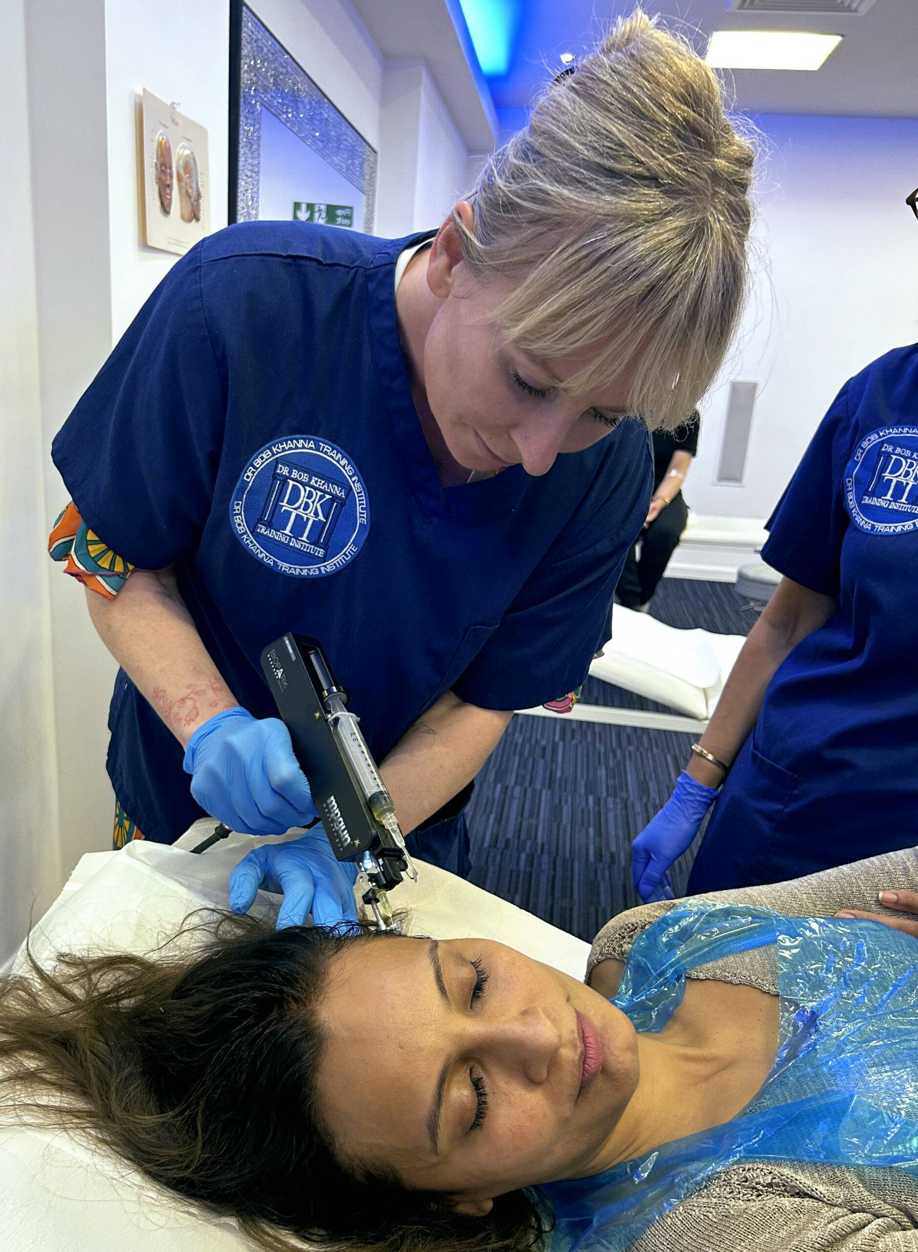 Image of a woman on a training course, injecting polynucleotides into a model's scalp for anti-hair loss