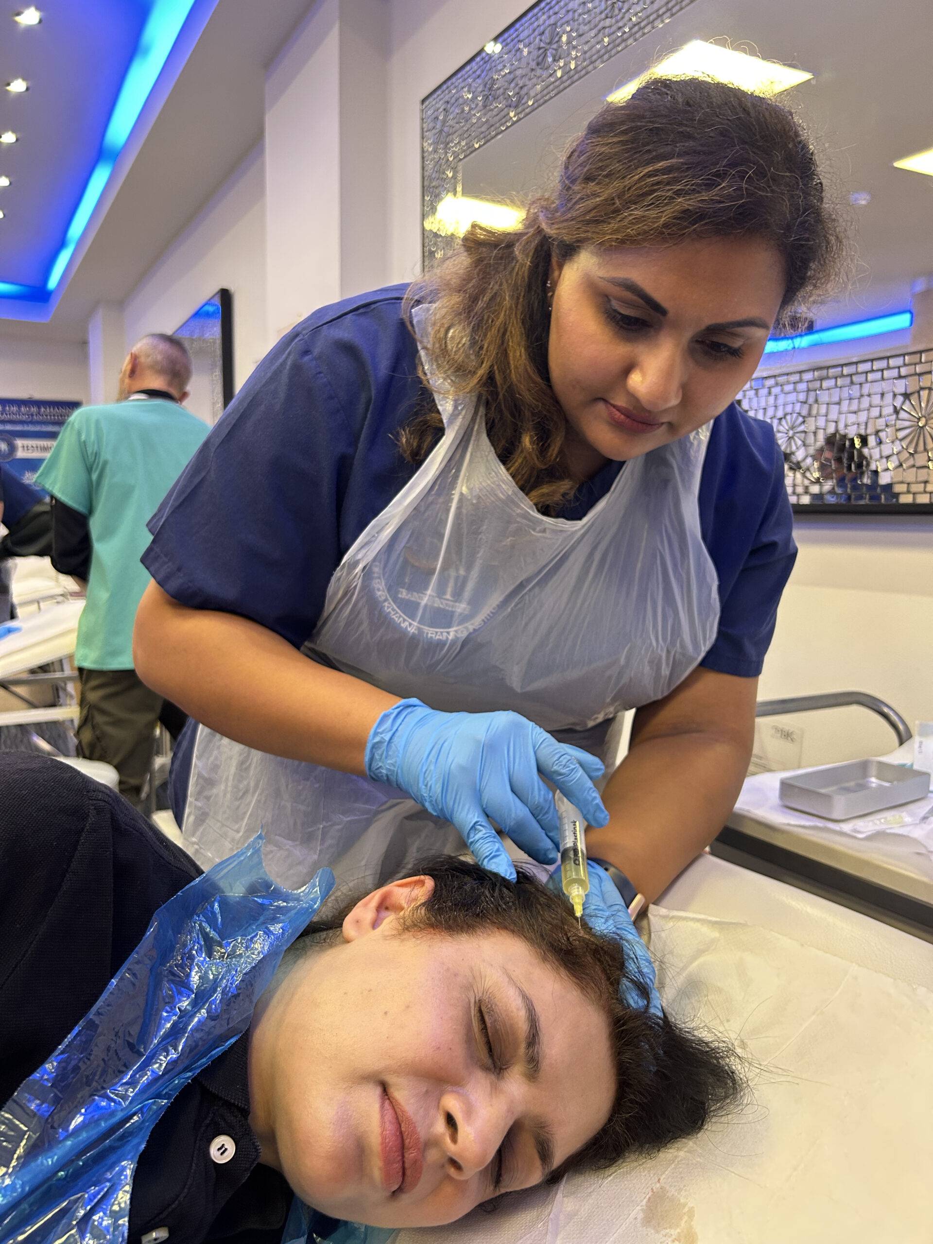 Image of a woman on a training course, injecting polynucleotides into a model's scalp for anti-hair loss